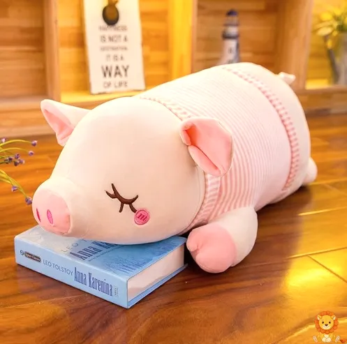 Entzückendes Plüschschwein mit weichem rosa Fell und einer kleinen rosa Schleife um den Hals, liegend auf einer weichen Decke. Perfekt zum Kuscheln und Liebhaben. - View 3